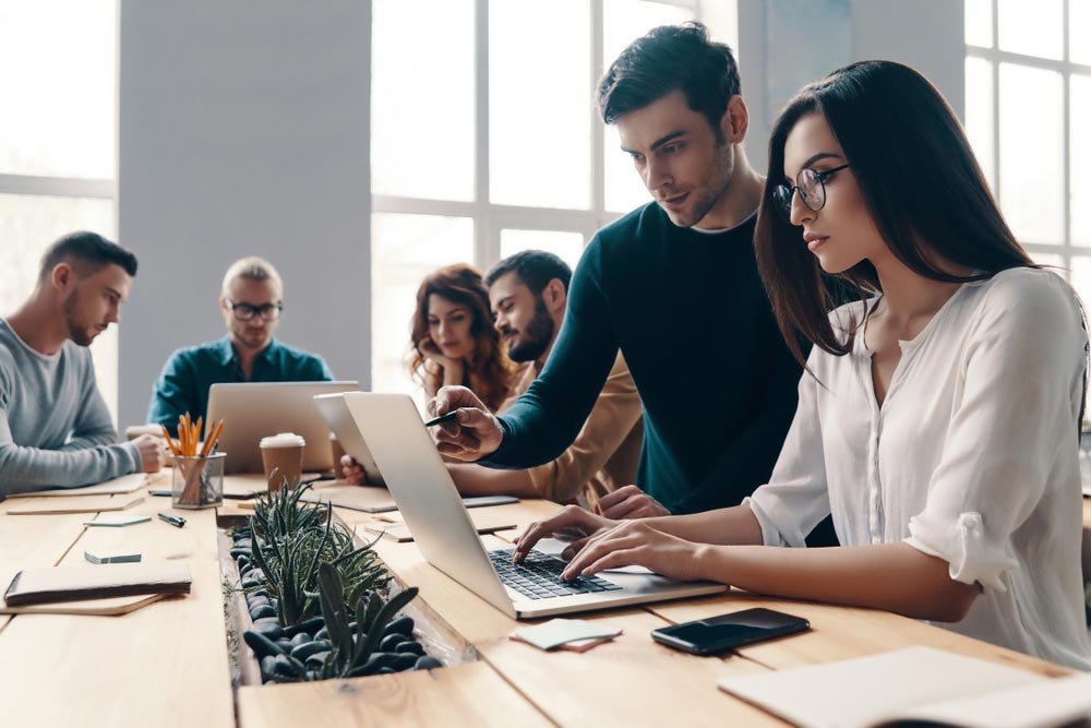 Group of young modern people in smart casual wear using modern technologies while working in the creative office